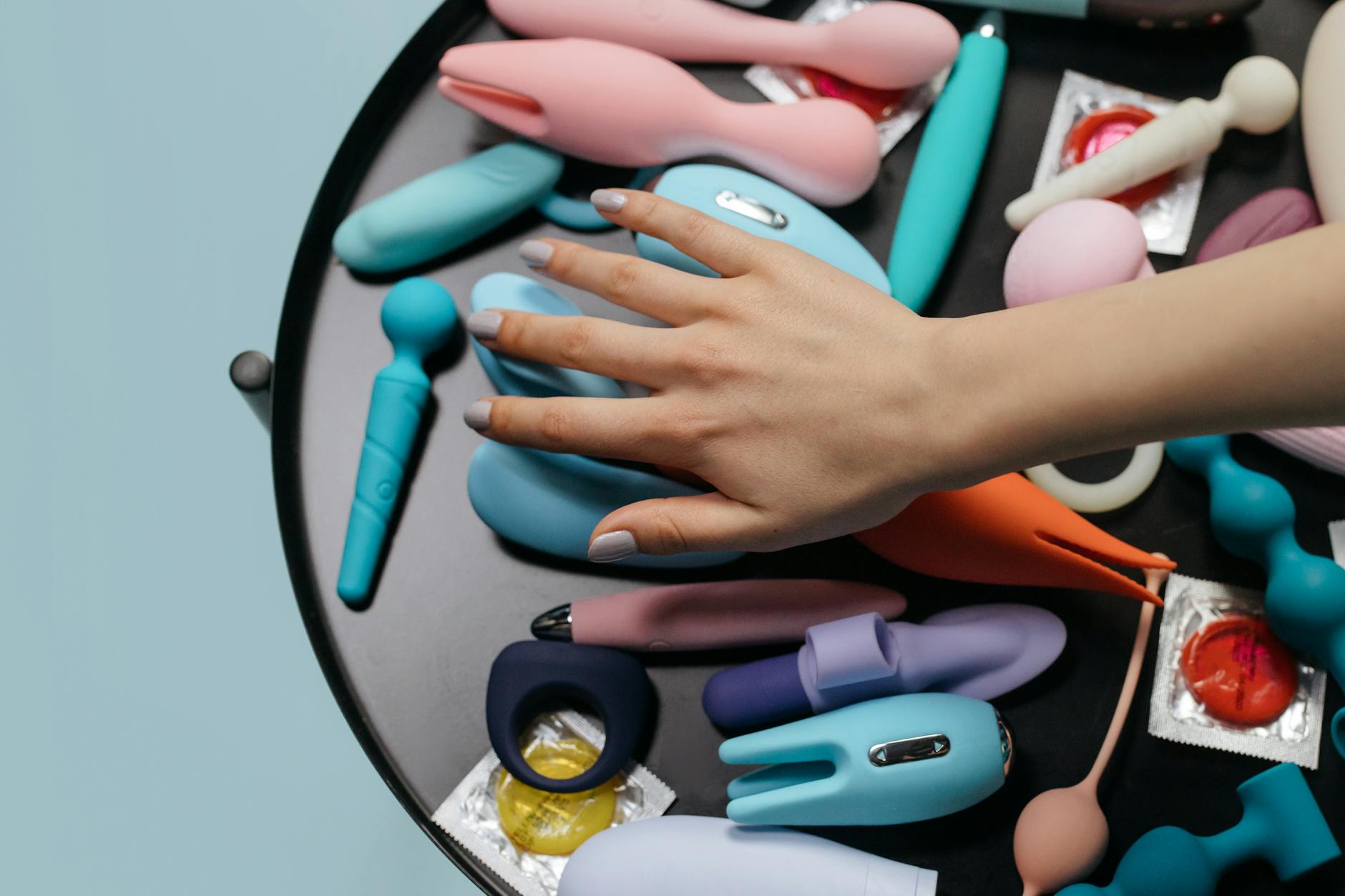 Eine Hand hält einen orangefarbenen Vibrator vor einem minimalistischen violetten Hintergrund