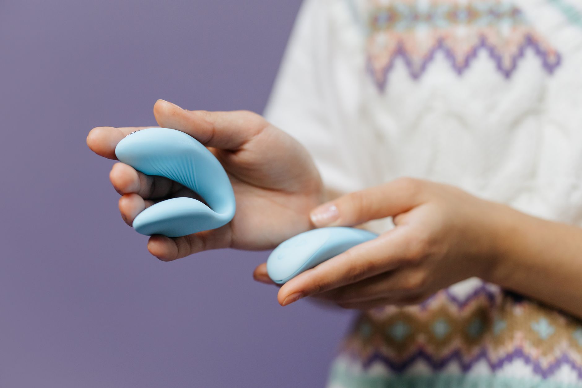 Close-up of hands holding a sleek vibrator against a purple background