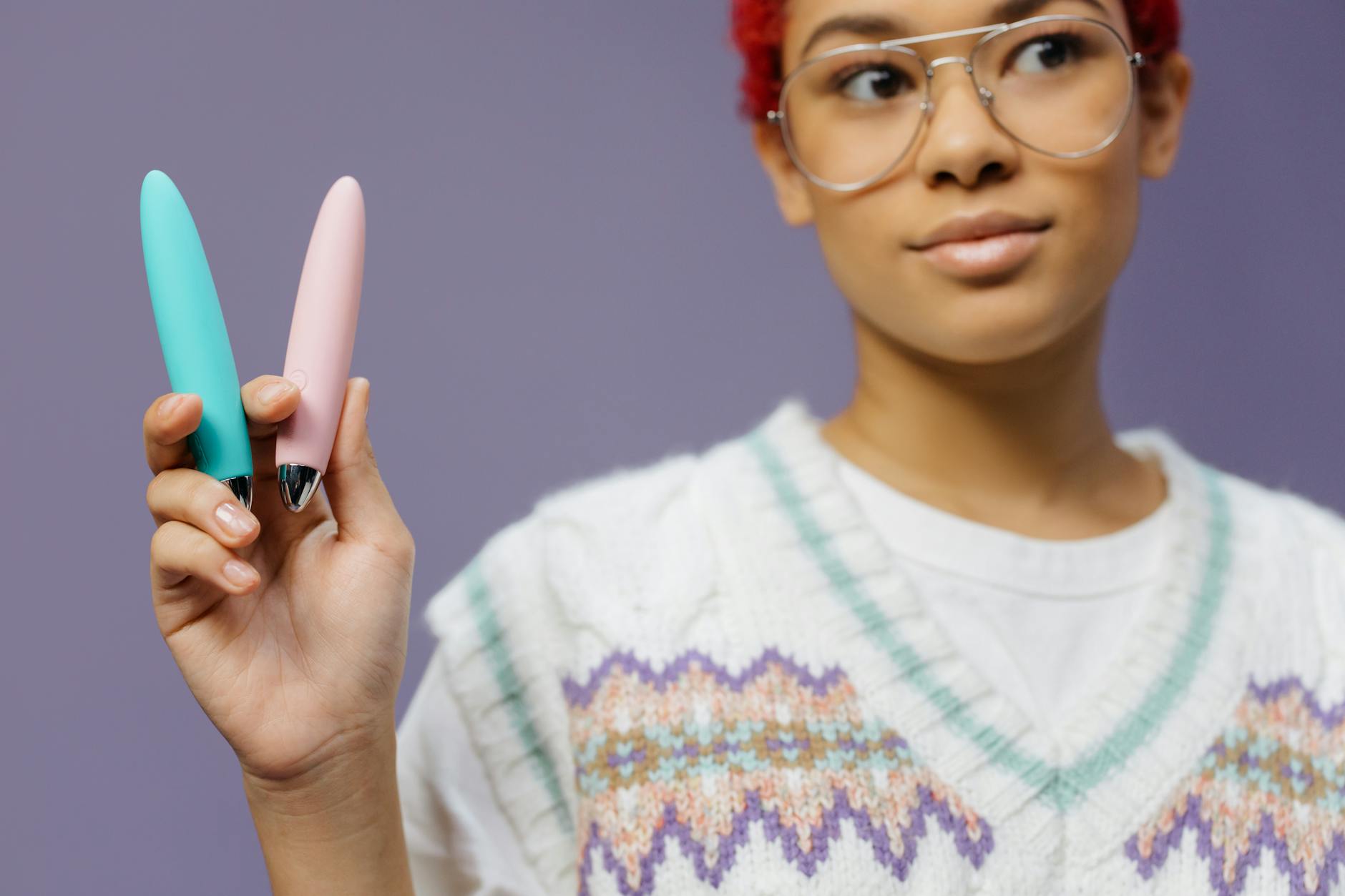 Frau mit Brille hält blue und pink Vibratoren in nachdenklicher Pose