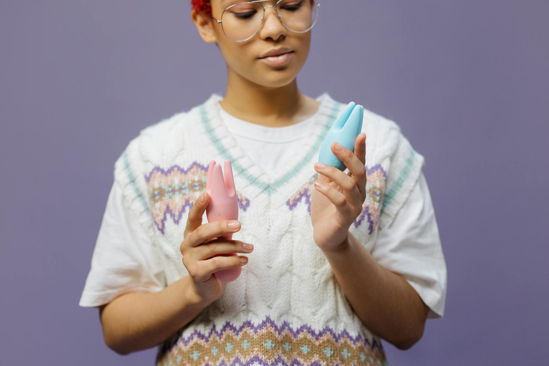 Frau mit Brille hält einen blauen und rosa Saugvibrator nachdenklich in den Händen