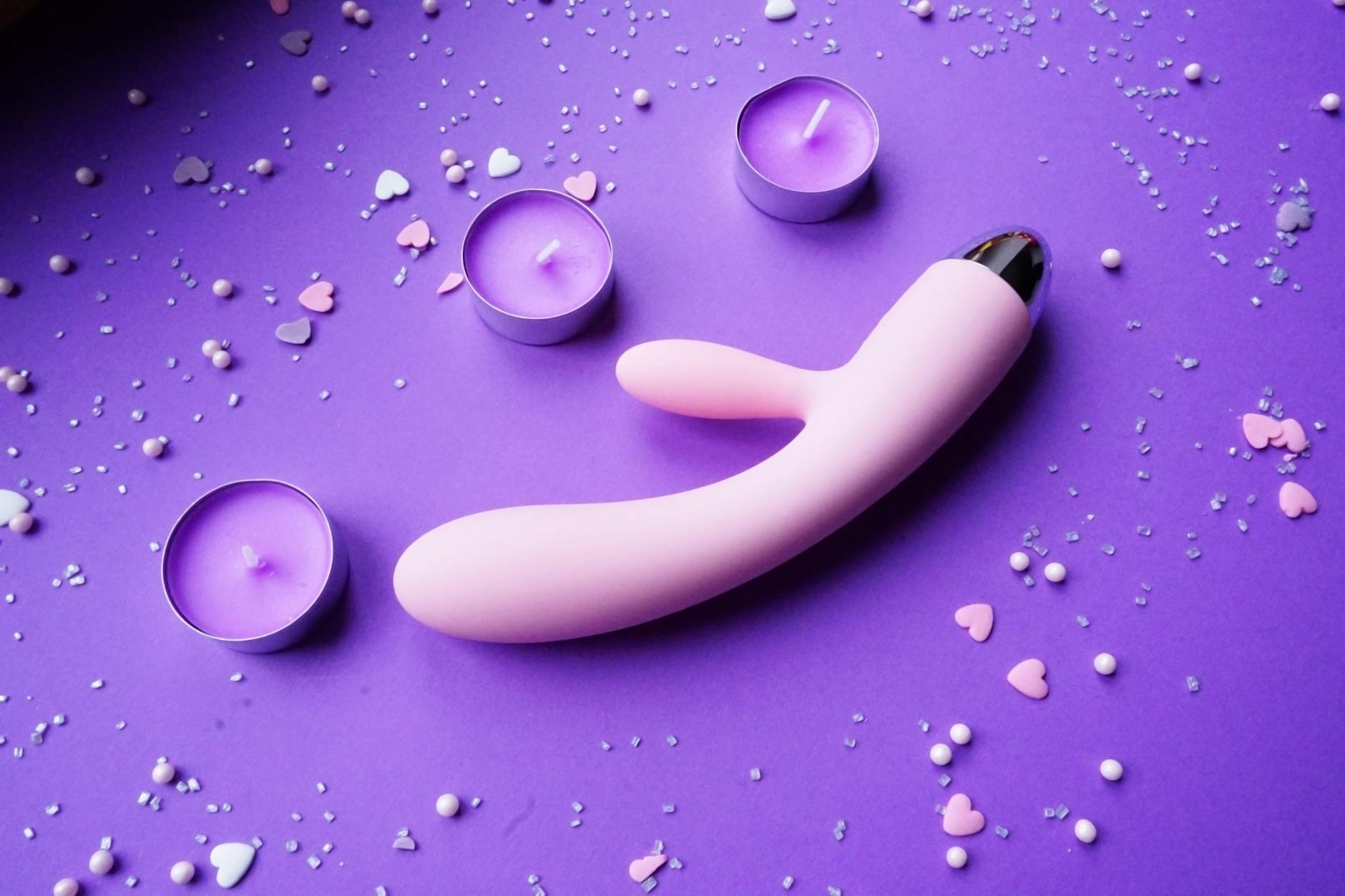 Pink vibrator on purple background with heart confetti and candles for romantic moment